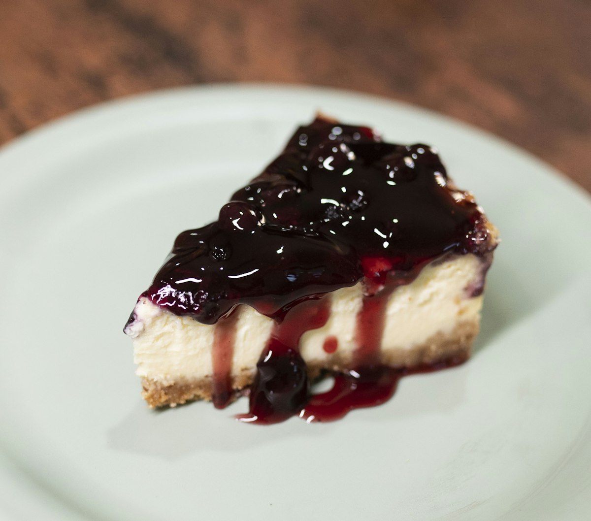 A slice of baked cheesecake under a dark berry compote